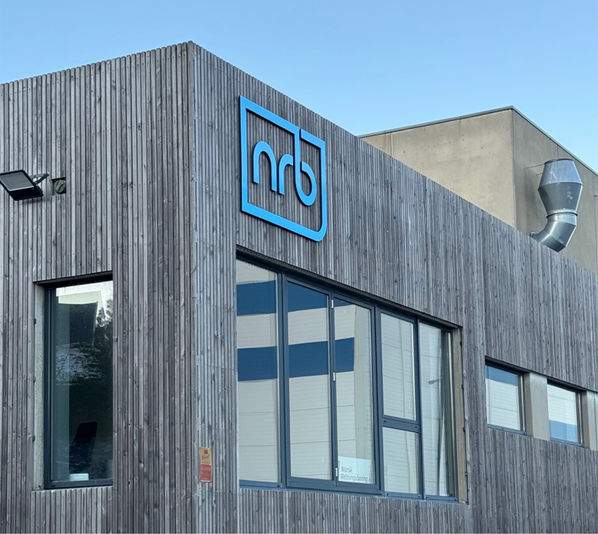 Kontorbygget til Norsk Retningsboring i Vestre Åmøy med blå firmalogo og store vinduer mot gateplan.